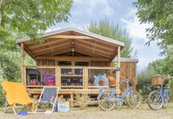 Cabina Cosyflower Premium con veranda in legno, sdraio, biciclette e attrezzatura estiva all'esterno.