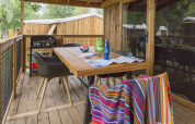Overdekt houten terras met tafel, stoelen, BBQ en gestreepte handdoek bij Cosyflower Premium, Camping Le Kerleyou.