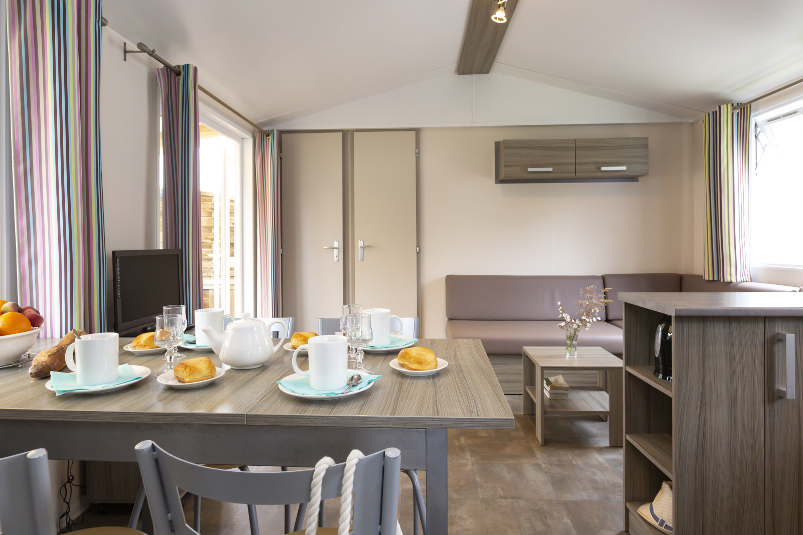 Moderne hutinterieur met ontbijttafel, zithoek en kleurrijke gestreepte gordijnen aan ramen.