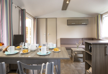 Interior de cabaña moderna con mesa preparada para desayuno, sala de estar y cortinas a rayas de colores.