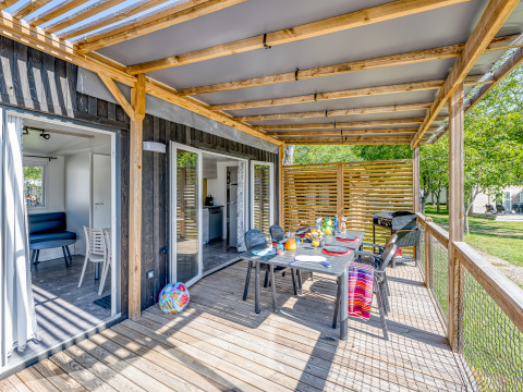 Outdoor deck at Homeflower Premium cabin with dining table, chairs, barbecue, and wooden pergola roof.