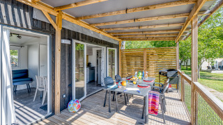 Veranda esterna della cabina Homeflower Premium con tavolo da pranzo, sedie, barbecue e pergolato in legno.