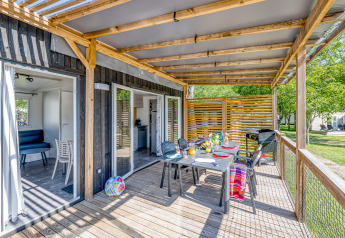 Veranda esterna della cabina Homeflower Premium con tavolo da pranzo, sedie, barbecue e pergolato in legno.