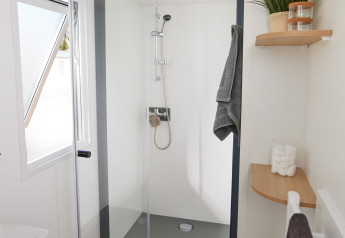 Bagno moderno nella cabina Homeflower Premium con doccia in vetro, pavimento in legno e scaffali eleganti.