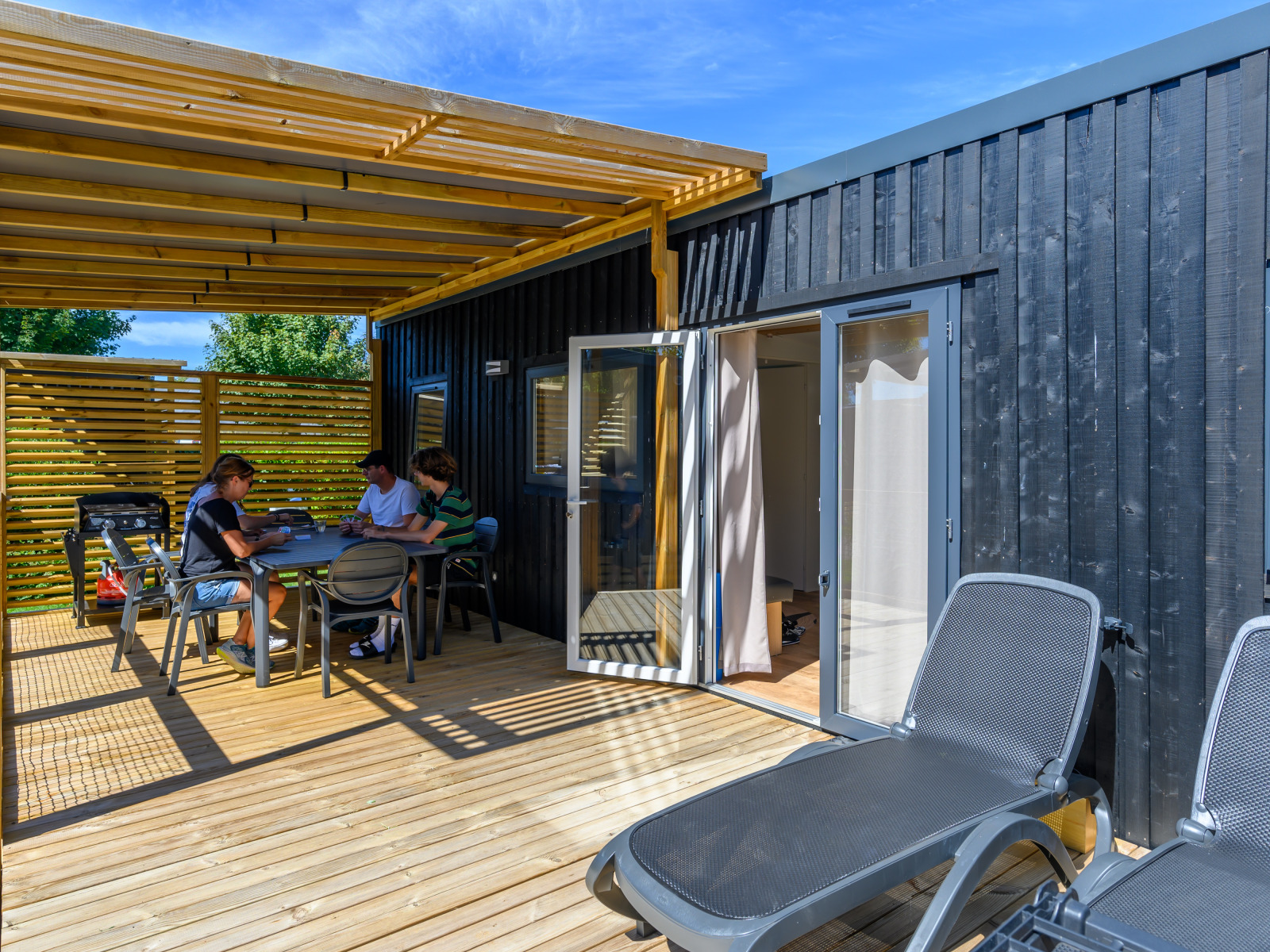 Buitenterras bij Homeflower Premium, Flower Camping Le Kerleyou, Frankrijk, met mensen aan tafel.
