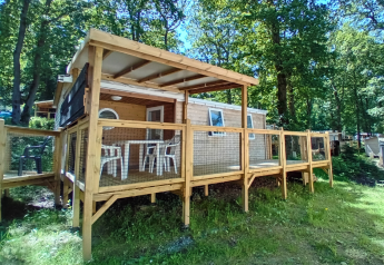 Außenaufnahme von Standaard Houten Stacaravan Mobilheim mit überdachter Terrasse im Waldgebiet.