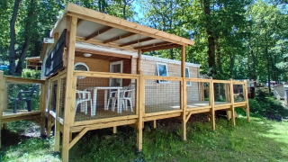 Buitenfoto van de Standaard Houten Stacaravan met overdekt terras in een bosrijke omgeving.