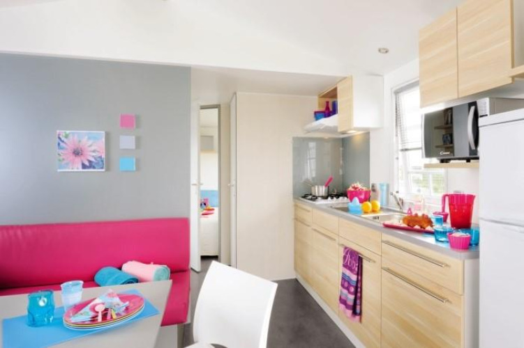 Cuisine moderne de glamping avec coin repas, armoires en bois clair et accessoires colorés.