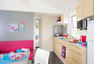 Cuisine moderne de glamping avec coin repas, armoires en bois clair et accessoires colorés.