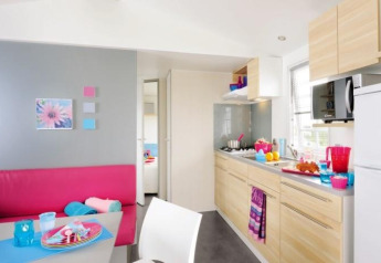 Cuisine moderne de glamping avec coin repas, armoires en bois clair et accessoires colorés.