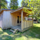Træhytte ved Chalet Bois Comfort med overdækket veranda, omgivet af frodige grønne træer og natur.