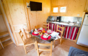 Cozy Chalet Bois Comfort interior at Flower Camping La Chênaie with dining table, kitchen, and TV.