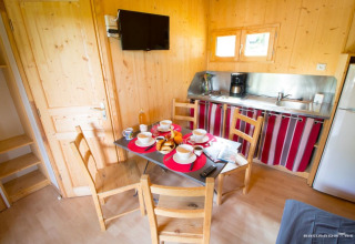 Intérieur du Chalet Bois Comfort à Flower Camping La Chênaie avec table à manger, cuisine et télévision.