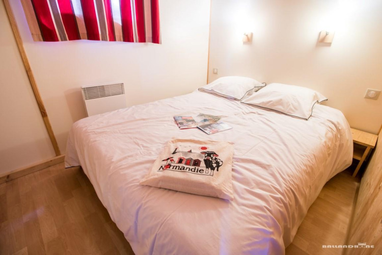 Gemütliches Schlafzimmer mit Doppelbett, weißer Bettwäsche und Souvenirkissen im Chalet Bois Comfort, La Chênaie.