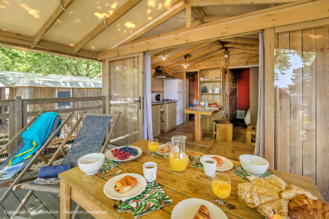 Petit-déjeuner en terrasse dans un lodge en bois avec intérieur cosy au Flower Camping La Chênaie en France.