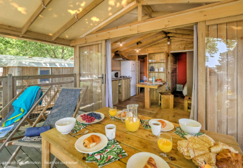Desayuno al aire libre en la terraza de una cabaña de madera en Flower Camping La Chênaie, Francia, con ambiente acogedor.