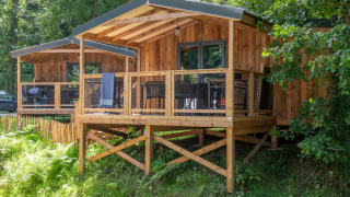 Elevated wooden cabins in a forested area, view from Lodge VIP Premium featuring deck and chairs.