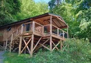 Wooden VIP lodge with terrace on stilts at Flower Camping La Chênaie in France, surrounded by lush forest.