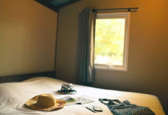 Cozy room at Lodge VIP Premium, Flower Camping La Chênaie, France, with hats, sunglasses, and a bag on bed.