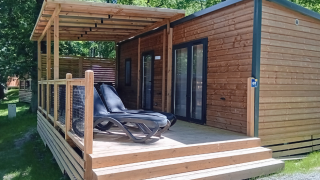 Homeflower Premium lodge with covered wooden deck and loungers, set among green trees in sunny weather.