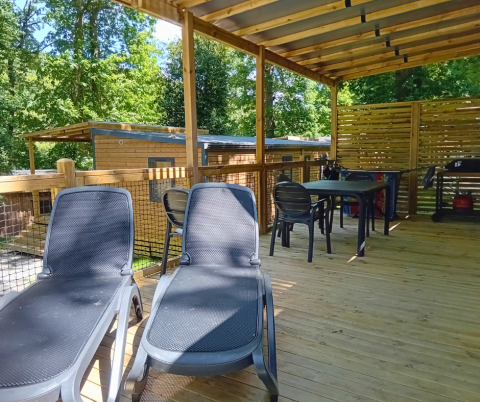Overdekt terras met zonnebedden en eettafel aan een Homeflower Premium lodge op Flower Camping La Chênaie, Frankrijk.