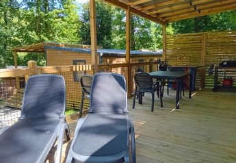 Terraza de madera techada con tumbonas y zona de comedor en Homeflower Premium, Flower Camping La Chênaie, Francia.