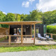 Udendørs foto af Homeflower Premium lodge med terrasse, to liggestole og gæster, omgivet af grøn skov.