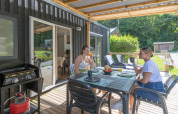 Two women enjoy drinks on the terrace at the Homeflower Premium lodge at Flower Camping La Chênaie in France.