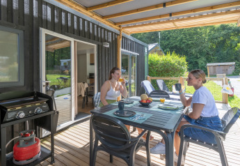 Two women enjoy drinks on the terrace at the Homeflower Premium lodge at Flower Camping La Chênaie in France.