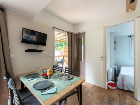 Modern glamping accommodation with dining table set, wall-mounted TV, and a glimpse into the bedroom.