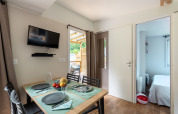 Moderne glamping-accommodatie met eettafel, wand-tv en een glimp van de slaapkamer met strandbal.