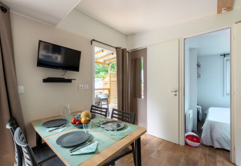 Modern glamping accommodation with dining table set, wall-mounted TV, and a glimpse into the bedroom.