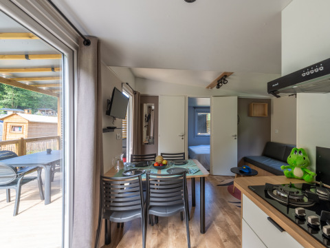 Modern glamping accommodation interior with dining table, kitchen, bedroom, and patio with forest view.