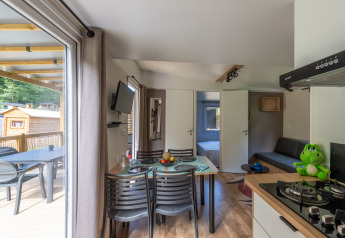 Modern glamping accommodation interior with dining table, kitchen, bedroom, and patio with forest view.