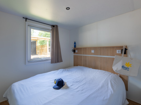 Glamping bedroom with a double bed, a window, a cap on the bed, and a tote bag hanging on the headboard.