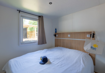 Glamping bedroom with a double bed, a window, a cap on the bed, and a tote bag hanging on the headboard.