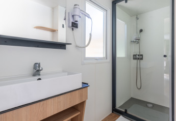 Bagno moderno e luminoso in una struttura glamping con doccia, lavandino, specchio e asciugacapelli.