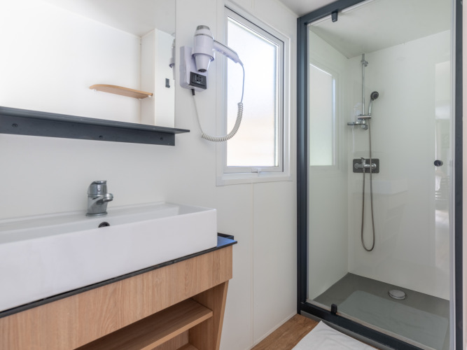 Bagno moderno e luminoso in una struttura glamping con doccia, lavandino, specchio e asciugacapelli.