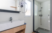 Salle de bain moderne et lumineuse dans un hébergement de glamping avec douche, lavabo et sèche-cheveux.