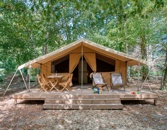 Tenda safari con veranda in legno, sedie da esterno e giochi, immersa nel verde della natura.