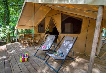 Safaritent met houten terras, relaxzetels en tafel bij Flower Camping La Sagne in Frankrijk.