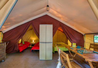 Interior de la Tente Safari Confort en Flower Camping La Sagne, Francia, con camas y mesa de madera.