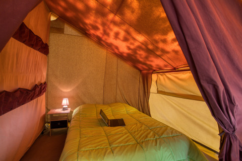 Interieur van een safaritent met bed en lamp bij Flower Camping La Sagne in Frankrijk, sfeervol verlicht.