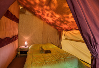 Interieur van een safaritent met bed en lamp bij Flower Camping La Sagne in Frankrijk, sfeervol verlicht.