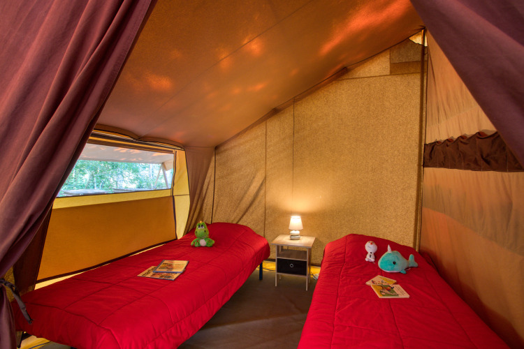 Inside a safari tent, Tente Safari Confort, with two single beds and lamp at Flower Camping La Sagne, France.
