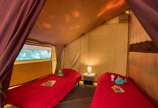 Binnenkant van de Safari Confort tent met twee bedden en lamp bij Flower Camping La Sagne in Frankrijk.