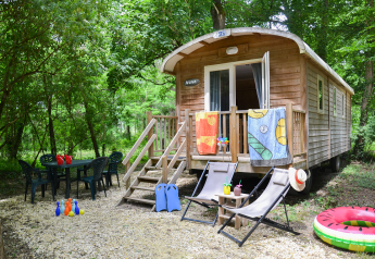 Roulotte Standard lodge in het bos, met stoelen, tafel, kinderspeelgoed en kleurrijke handdoeken buiten.