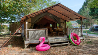 Safaritent Freeflower Confort met houten veranda, tuinmeubels en opblaasbare zwembadringen buiten.