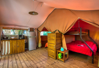 Interieur van een gezellige safaritent met keuken, koelkast, houten vloer en stapelbed bij Flower Camping La Sagne.
