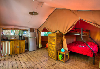 Interno di una tenda safari accogliente con cucina, frigorifero, pavimento in legno e letto a castello al Flower Camping La Sagne.